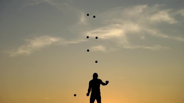 Circus artist juggling with balls on colorful sunset