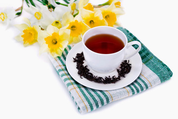 Black tea in a cup on green textile napkin with yellow daffodil flowers isolated on a white background.