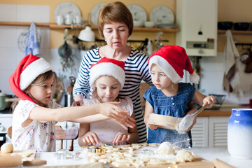 Family is cooking Christmas cookies together in cozy home kitchen for holiday dinner. Funny kids and woman are baking Xmas cake. Mother is teaching daughters. Lifestyle moment. Children chef concept.