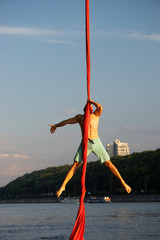 Muscular male circus artist doing crazy trick with aerial silk on a sky and river background