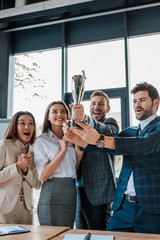Obraz premium happy multicultural businesswomen and businessmen looking at trophy in office