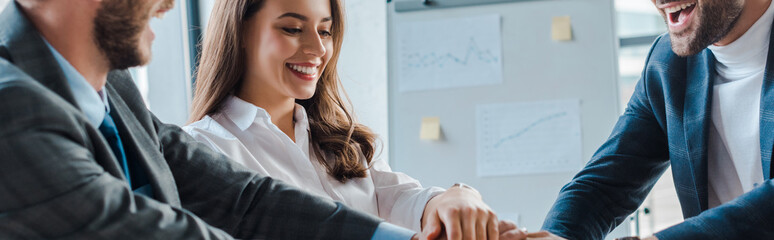 panoramic shot of happy businessmen and businesswoman putting hands together