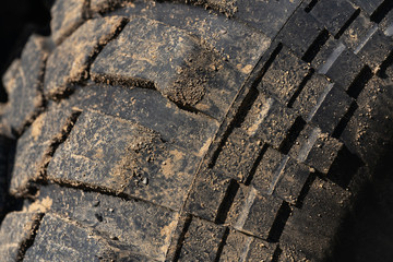 Old used rubber extreme terrain tire with worn wear-resistant tread. Close-up of black muddy off-road tire on 4x4 automobile with adhering dirt after overcoming an impassable mountain off-road trip.