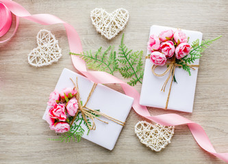 Composition with gift boxes decorated with grin branch, rose, wooden hearts and satin pink ribbon.