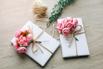 Handmade present box wrapped in paper with branch of roses. Eucalyptus branch and rustic hemp cord spools on background