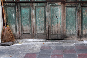 The ancient green wooden door is closed and has two brooms leaning on its side