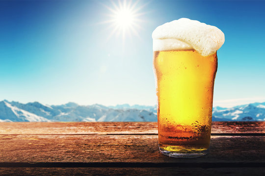 apres ski - cold beer glass on the table with sunny winter mountains landscape at ski resort. copy space