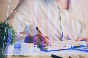 Double exposure of man's hands writing notes of stock market with forex chart.