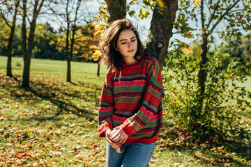 Image of romantic beautiful young woman wearing sweater enjoying the weather in the city park. Pretty femaleresting outside.