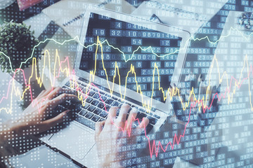 Double exposure of man's hands writing notes with laptop of stock market with forex graph background. Top View. Concept of research and trading.