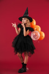 Cute little girl wearing Halloween witch costume standing