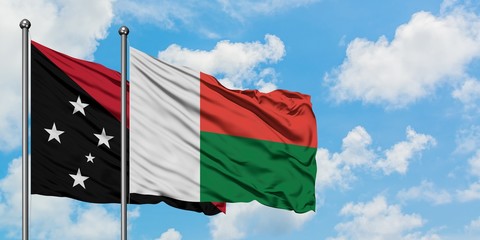 Papua New Guinea and Madagascar flag waving in the wind against white cloudy blue sky together. Diplomacy concept, international relations.