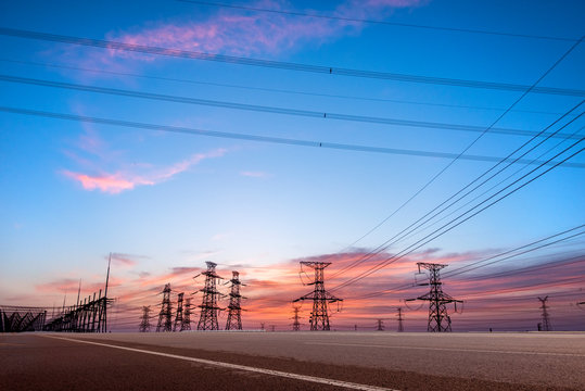 Transmission tower on asphalt road in the setting sun
