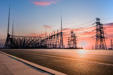 Fototapeta na wymiar Transmission tower on asphalt road in the setting sun