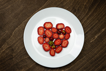 Creative Valentine Day romantic concept composition flat lay top view with heart strawberries on a white plate on a wooden table.