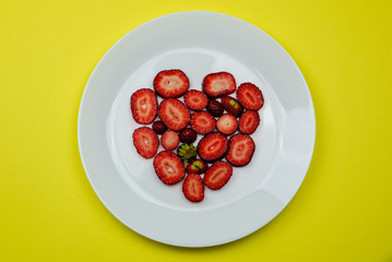 Creative Valentine Day romantic concept composition flat lay top view with heart strawberries on a white plate isolated on a yellow background.
