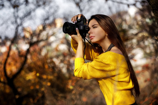 young woman photographer with professional camera takes pictures in nature. space for text