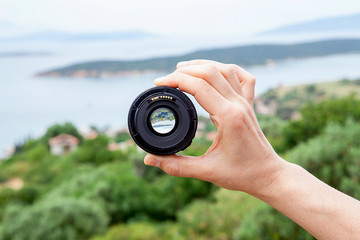 Photo camera lens of among seacoast mountains and trees. Seascape.
