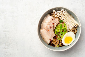 Asian soup ramen with noodles, pork, spring onion, enoki mushrooms and boiled egg in bowl on concrete background. Top view. Copy space.