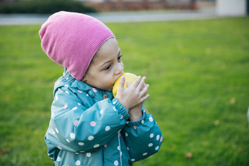 Little lovely girl on a walk eats an apple, a child eats healthy food, a happy kid walks on an autumn day