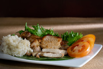 Fried pork with organic vegetable in white dish and sticky rice in bamboo cup on brown tablecloth