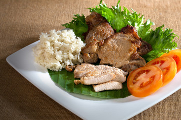 Fried pork with organic vegetable in white dish and sticky rice in bamboo cup on brown tablecloth