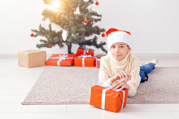 Fototapeta na wymiar Holidays, christmas, childhood and people concept - smiling happy teen boy in santa hat with gift box over christmas tree background