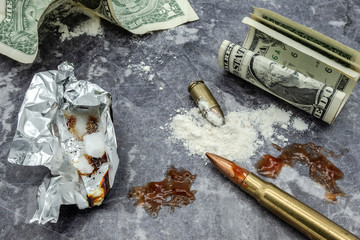 Fototapeta na wymiar Mock-up concept of illegal drug dealing on a work surface. Showing dollar bills, mock-up bullets together with prop blood together with smoking foil.
