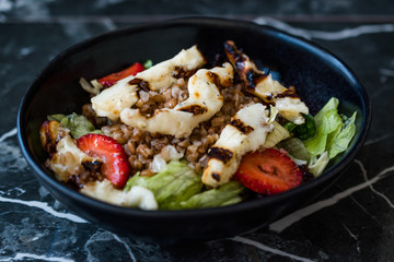 Grilled Halloumi Cheese Salad with Strawberry Slices and Buckwheat / Hellim in Black Bowl on Dark Granite Surface.
