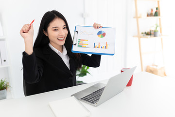 Obraz na płótnie Canvas asian female officer holding presentation board, she sitting and show cheer emotion, she use laptop and thinking to plan, she feeling happy and smile, happiness organisation and congratulation time