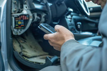 male mechanic looks at the phone information about the cause of the breakdown of the car sitting next to the car. Concept of car repair