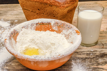 Fresh bread brick on the table closeup. Next is a bowl of flour and egg, a glass of milk.