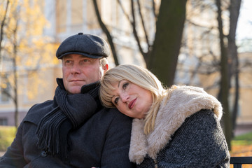 Closeup portrait of happy blonde mature woman and beautiful middle-aged brunette, looking away. Loving couple of 45-50 years old walks in autumn park in warm clothes, in coat and enjoys life