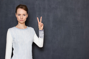 Portrait of serious focused young woman showing peace gesture