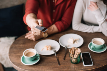 cropped view of young couple eating cheesecake and drinking coffee while man holding credit card in coffee shop