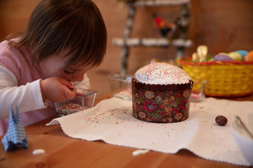 Toddler girl eating colorful sugar balls after finishing decorating Easter cake