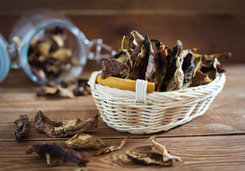 Sliced dried mushrooms lie in a small wicker basket on a wooden table close-up