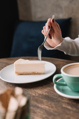 cropped view of woman eating cheesecake with fork and drinking coffee in cafe