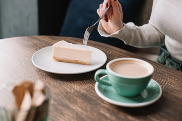 partial view of woman eating cheesecake with fork and drinking coffee in cafe