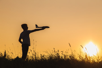 Black silhouette of young white kid holding toy plastic blue plane in hand. Confident boy setting big goals concept. Horizontal color photography.