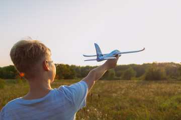 Closeup back view of confident cute little kid holding big toy plane in hand isolated at sunny orange sunset sky background. Horizontal color image.