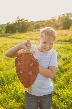 Closeup portrait of happy cheerful smiling white kid playing happily outdoor holding wooden sword and shield in hands. Vertcial color photography.