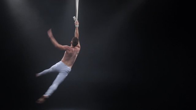 Muscular circus aerialist on the aerial straps in black studio