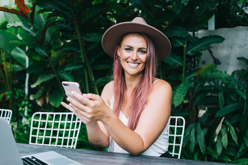 Fototapeta premium Smiling woman browsing cellphone on greenery background
