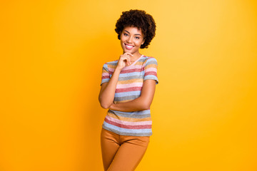 Photo of cheerful cute nice charming positive girl wearing pants trousers striped t-shirt smiling toothily isolated over vivid yellow color background in a fit of brainstorming