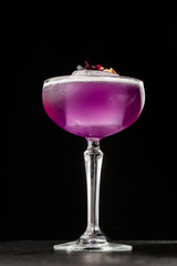 Homemade Purple Cocktail with a Large Ice Cube on black background. Close up of purple cocktails in a glass of margaritas with sugar edges, violet and protein foam. Vertical photo.