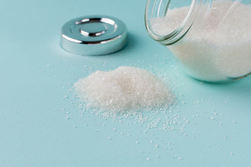 Glass jar with sugar upside down. Sugar rushes out of the jar on a blue background.