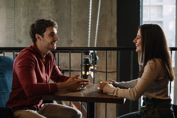 smiling young couple looking at each other while talking on balcony in coffee shop