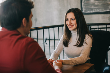 smiling young woman looking at boyfriend and holding his hands on balcony in coffee shop