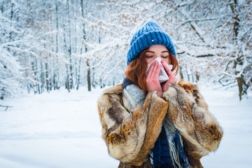 portrait of a young woman in the winter forest. a beautiful girl sneezes into a napkin. get sick in...